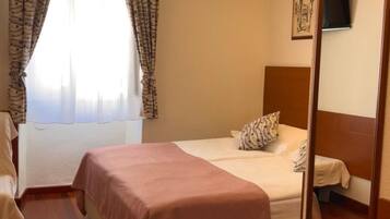 Habitación de hotel con cama, escritorio, silla, televisor montado en la pared y ventana con cortinas.
