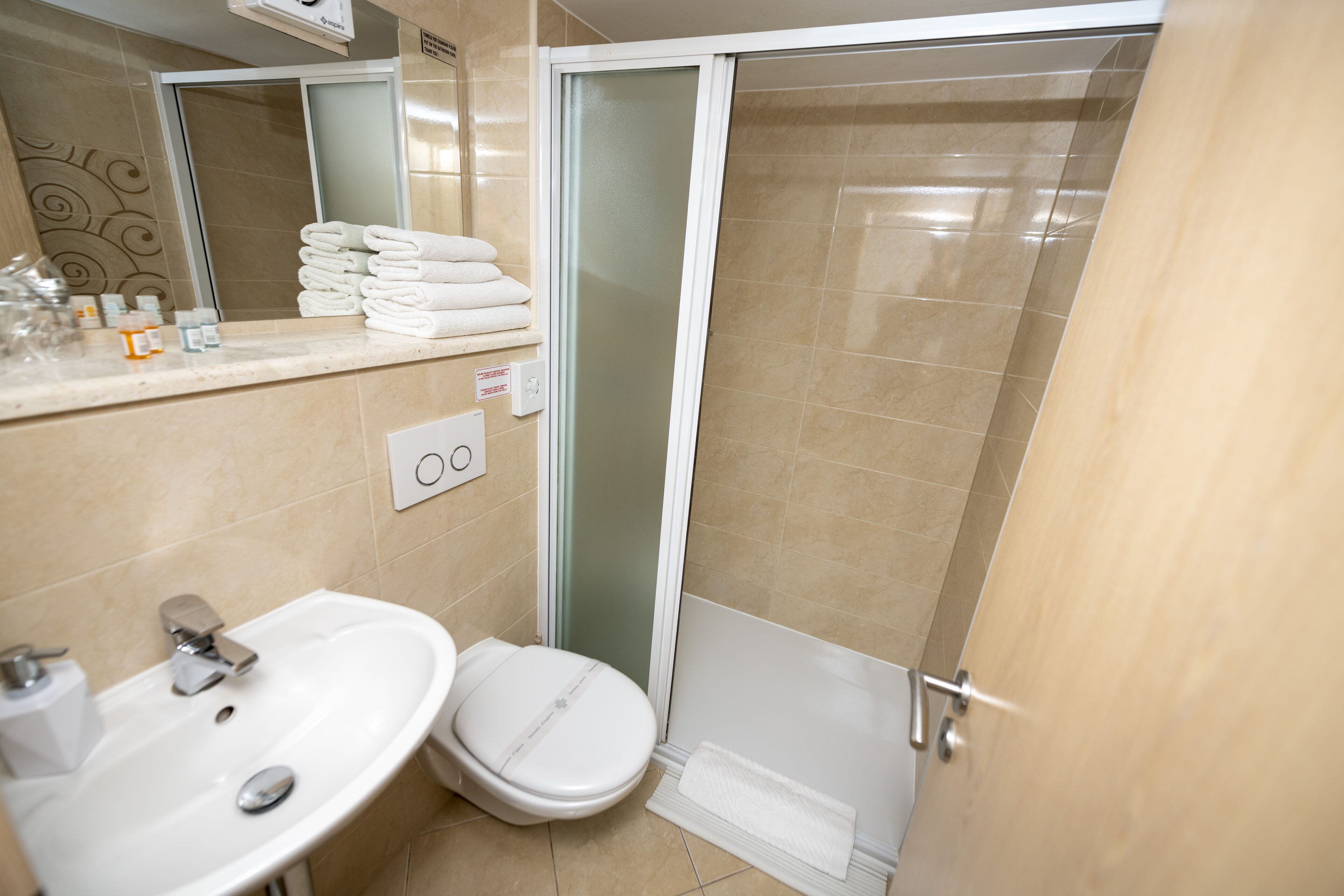 A bathroom with a sink, toilet, and shower. There are towels stacked on the wall and a mirror above the sink.
