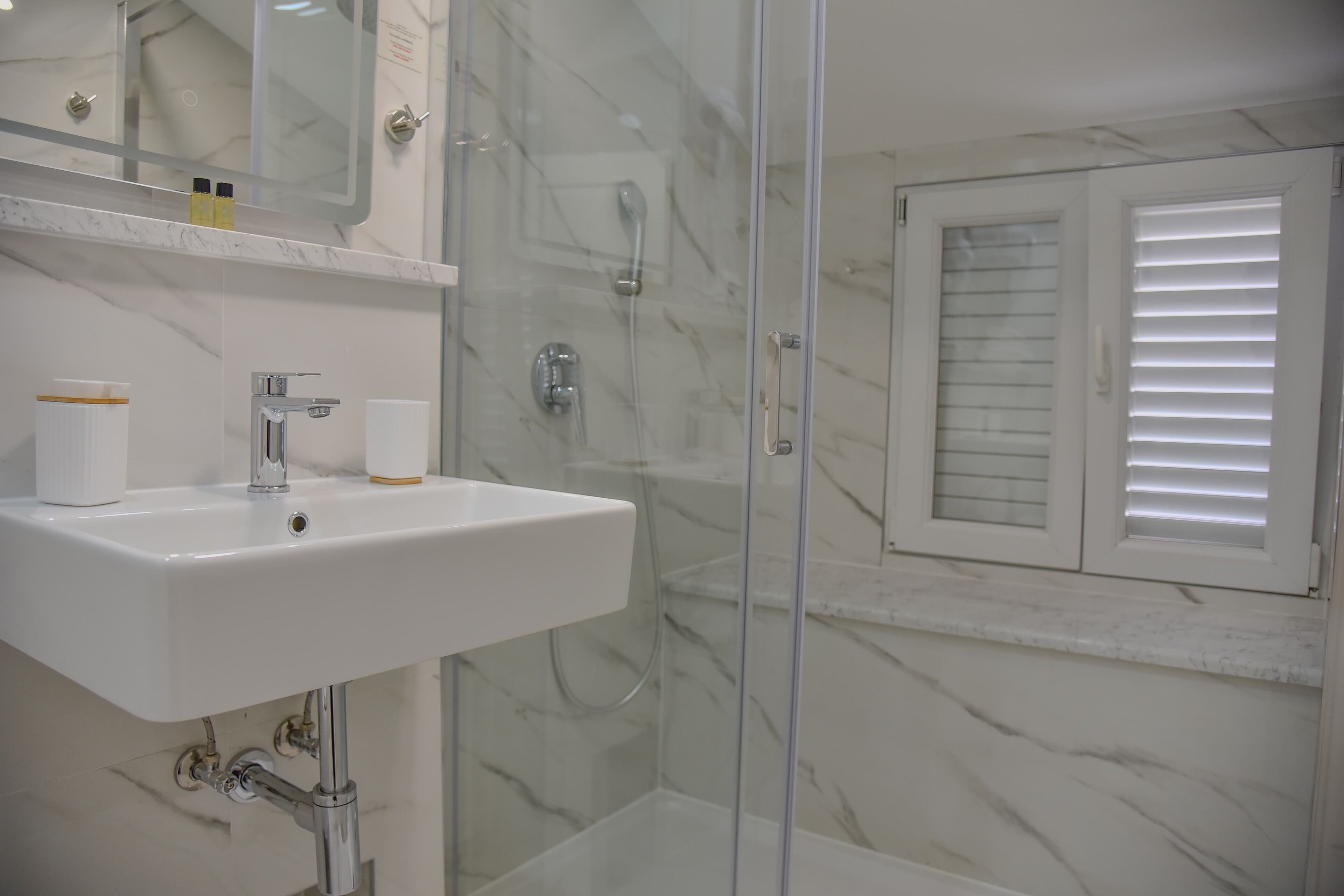 A bathroom with a white sink, a glass shower enclosure, and a window with blinds.
