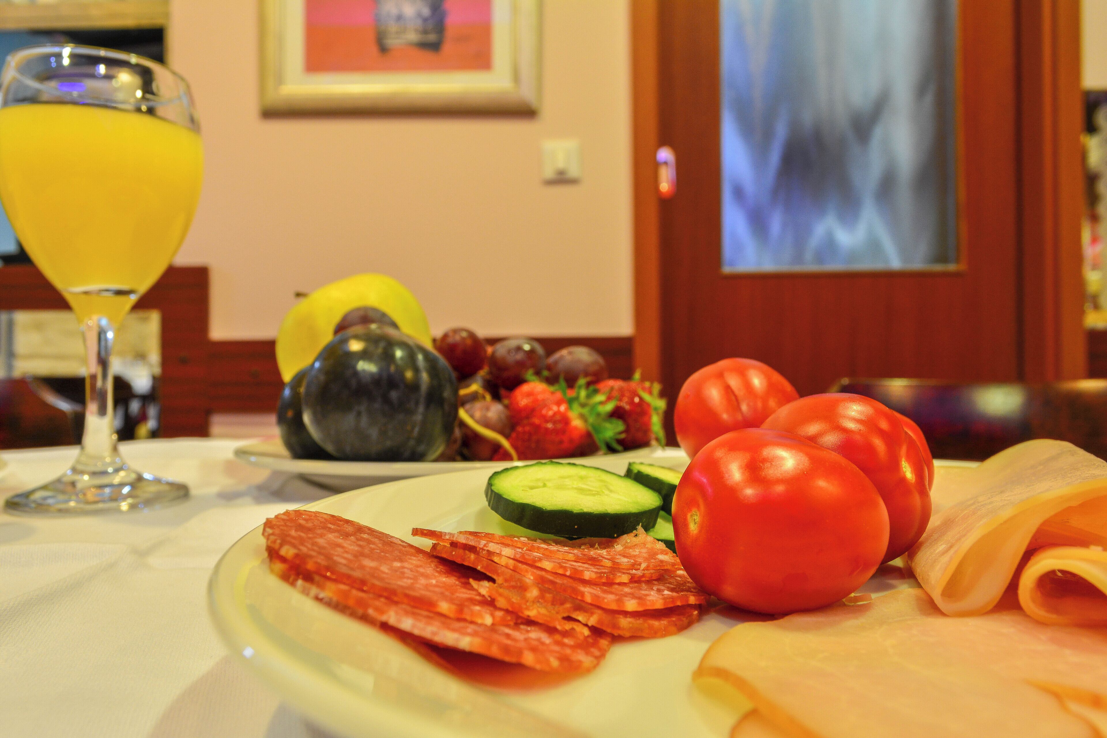 A plate of food including sliced salami, cheese, tomatoes, cucumbers, and grapes, with a glass of orange juice on a table.