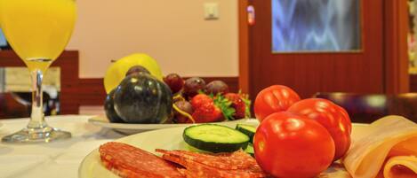 A plate of food including sliced salami, cheese, tomatoes, cucumbers, and grapes, with a glass of orange juice on a table.