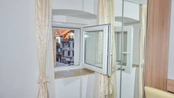 A room with a window, a mirror, and a view of buildings outside.