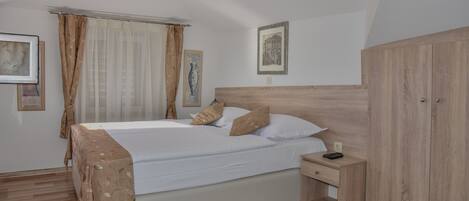 A neatly made bed with a headboard, a bedside table with a remote control, and a wardrobe.