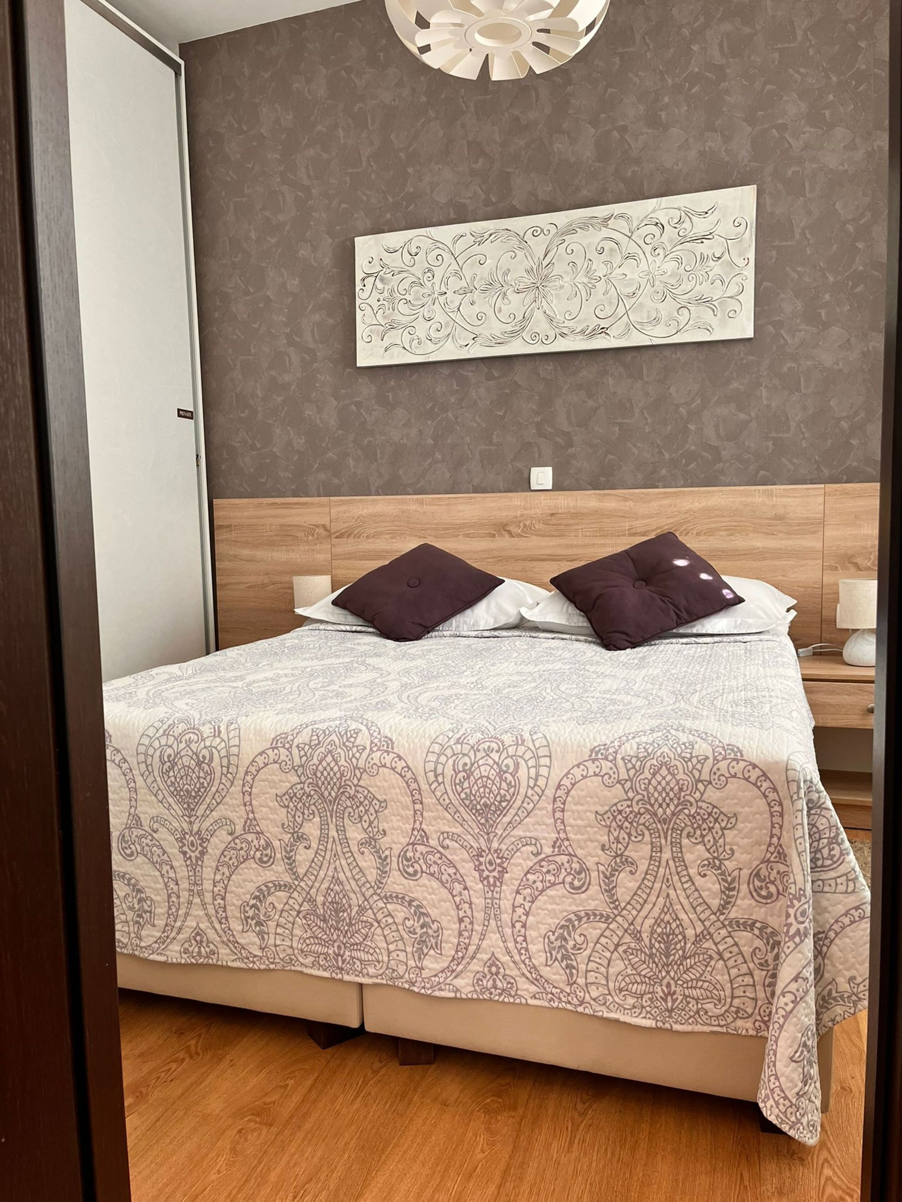Ein ordentlich bezogenes Bett mit einem gemusterten Überwurf, einem Kopfteil und zwei Kissen.