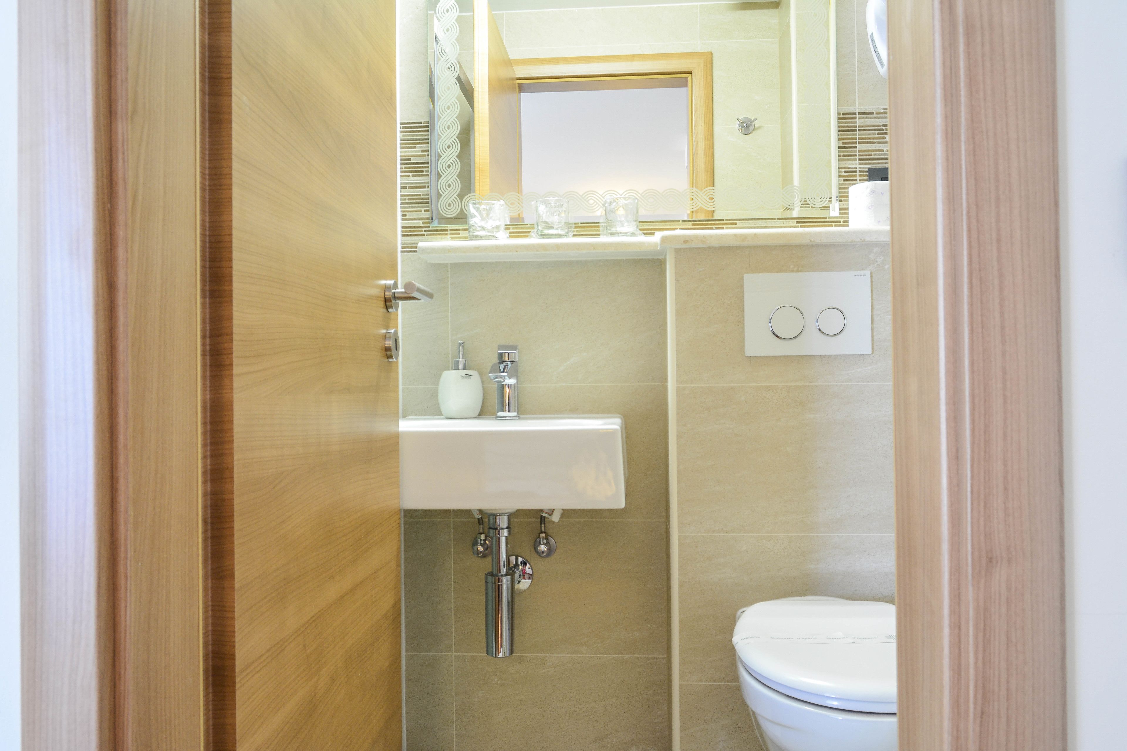 Een badkamer met een houten deur, een witte wasbak, een spiegel en een toilet.