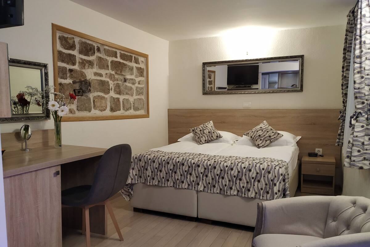 Hotellihuone, jossa on sänky, työpöytä, tuoli, televisio ja kiviseinäkoriste.