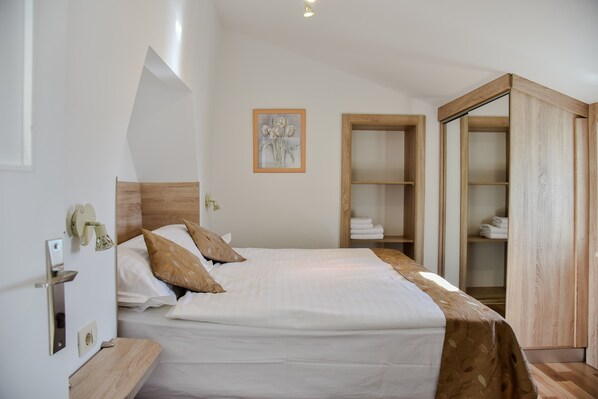 Un lit bien fait, avec une tête de lit, une armoire en bois et une œuvre d’art encadrée accrochée au mur.