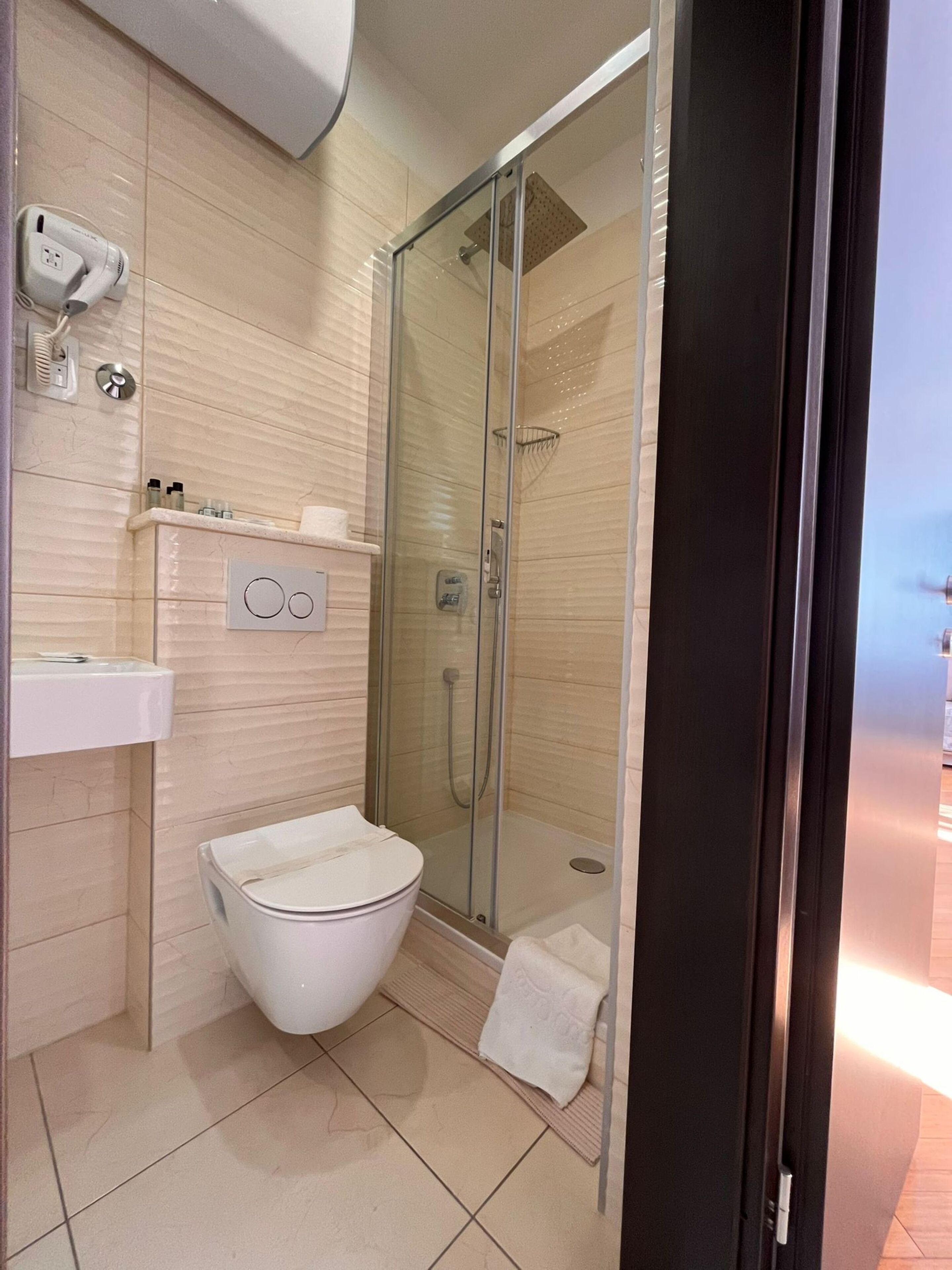 Un baño moderno con ducha de vidrio, inodoro blanco y lavabo con toallero.