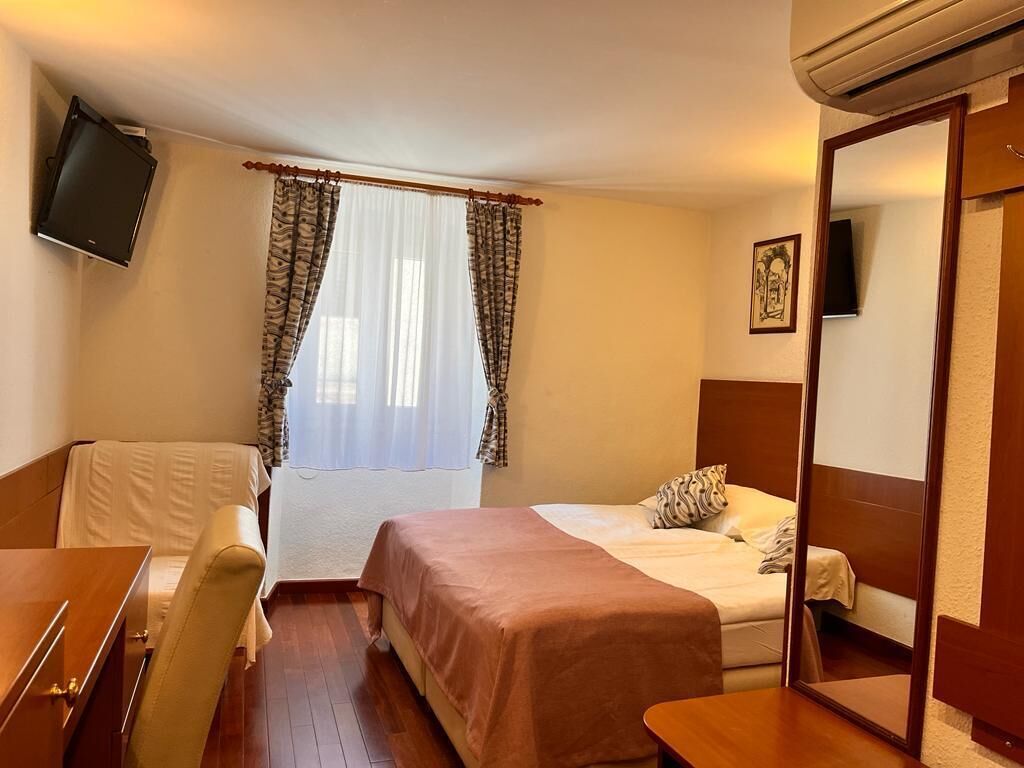 Quarto de hotel com cama, escrivaninha, cadeira, televisão e guarda-roupa.