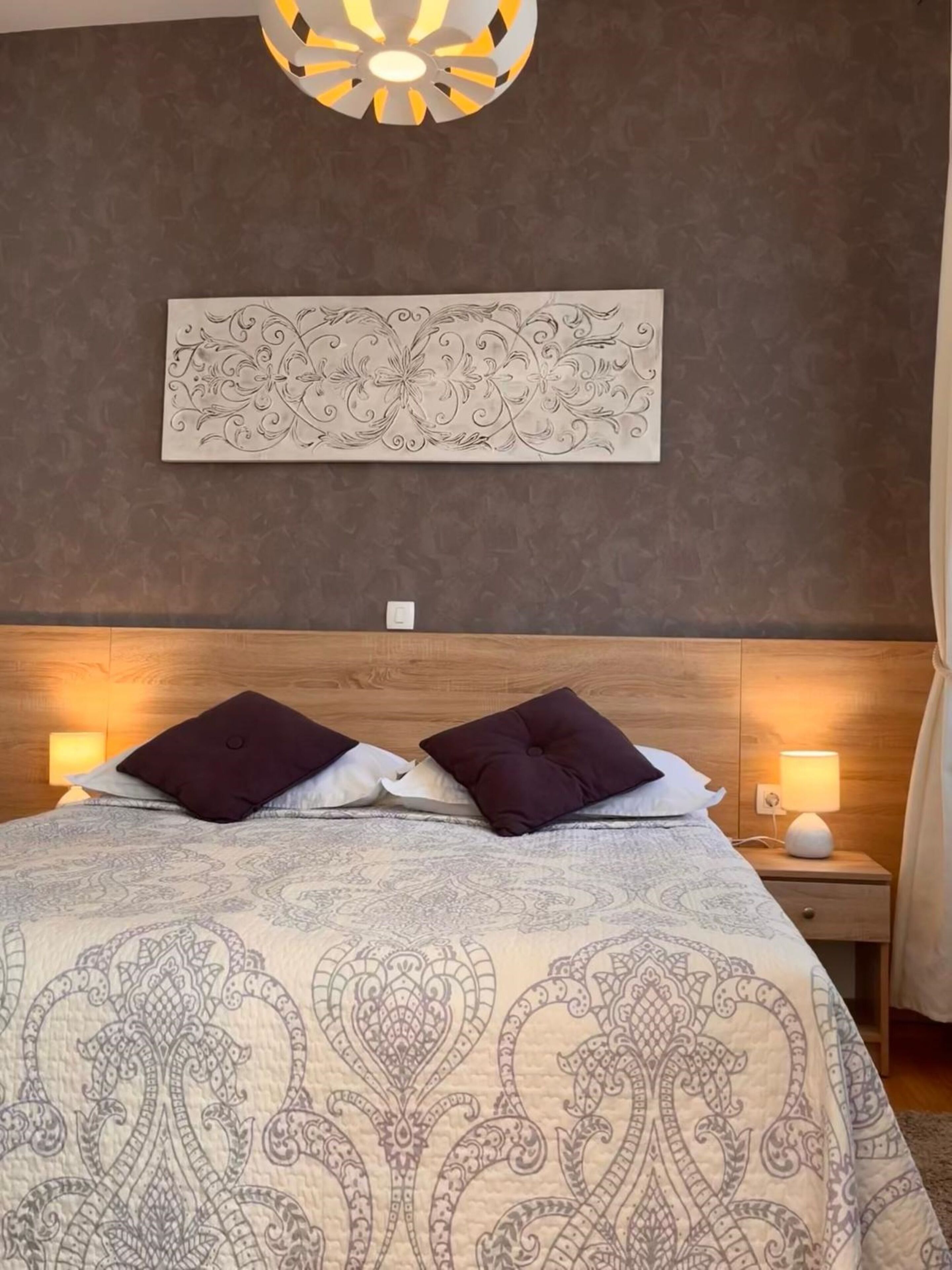 Ein Schlafzimmer mit einem großen Bett, zwei Nachttischlampen, einem Wanddekor und einem Holz-Kopfteil.