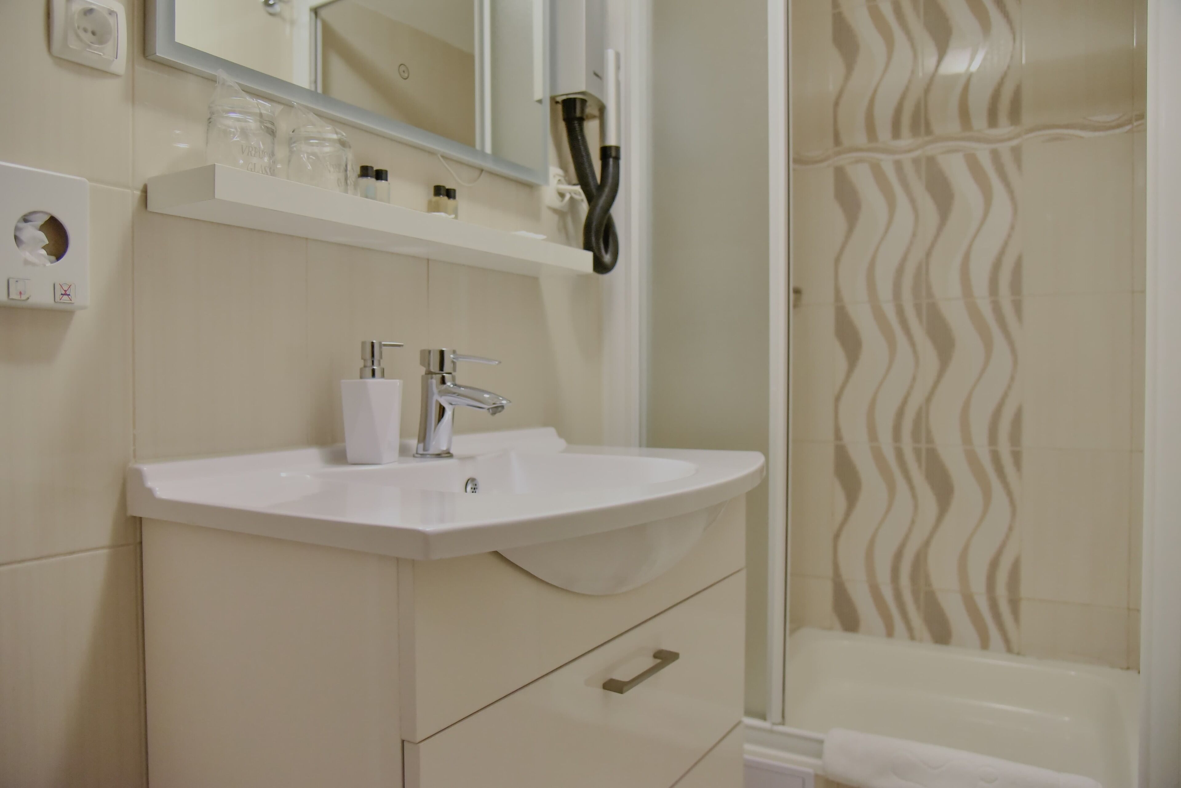A bathroom with a white sink, mirror, and towel rack. There is a shower with a wavy tile pattern.