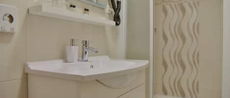 A bathroom with a white sink, mirror, and towel rack. There is a shower with a wavy tile pattern.