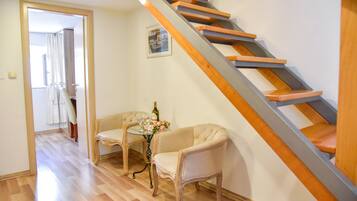 A staircase with wooden steps and a metal handrail, leading to an upper floor. There is a small table with a bottle and glasses, and two chairs in the foreground.