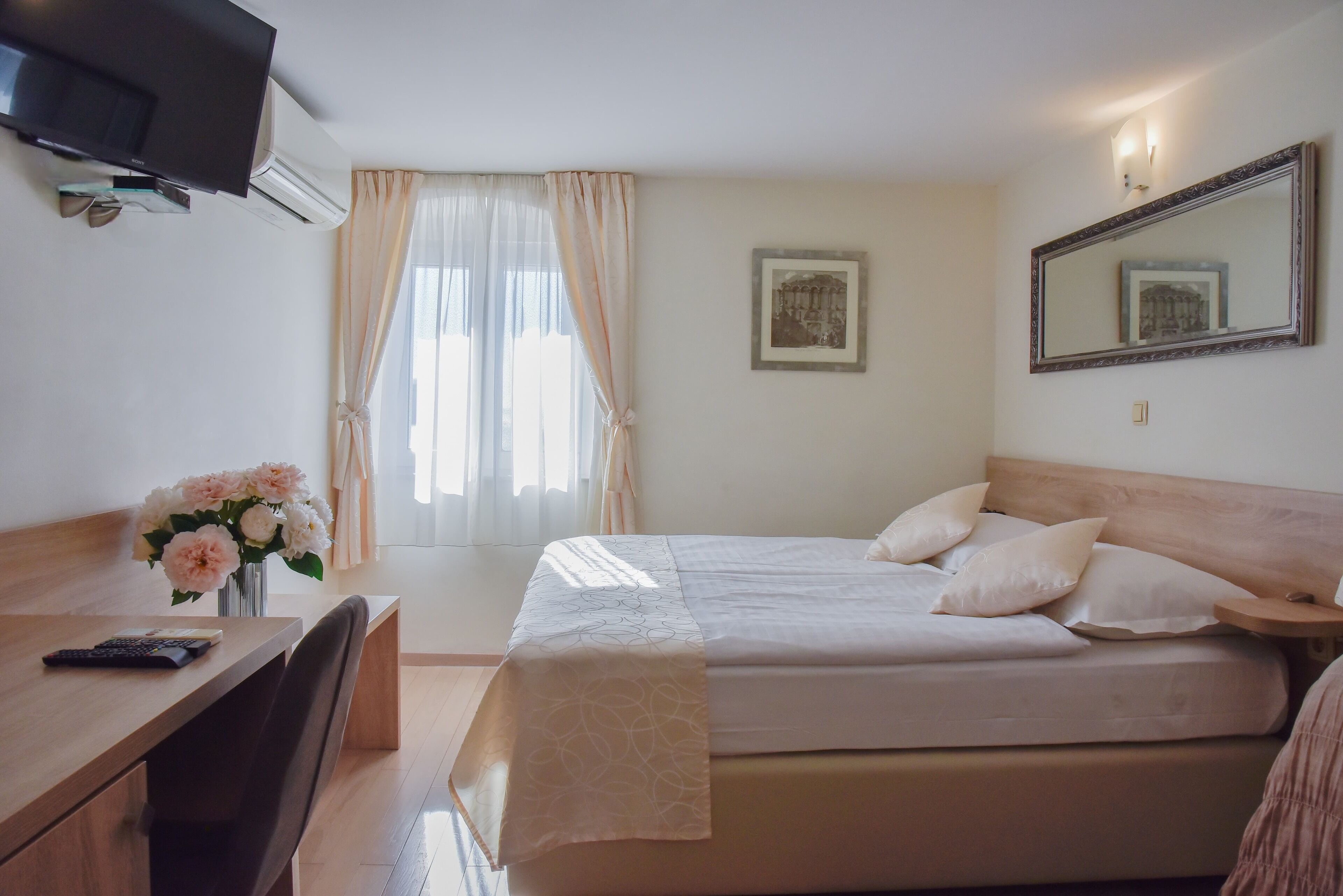 A hotel room with a bed, a desk with a chair, a TV, and a window with curtains.