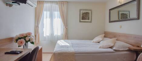 A hotel room with a bed, a desk with a chair, a TV, and a window with curtains.