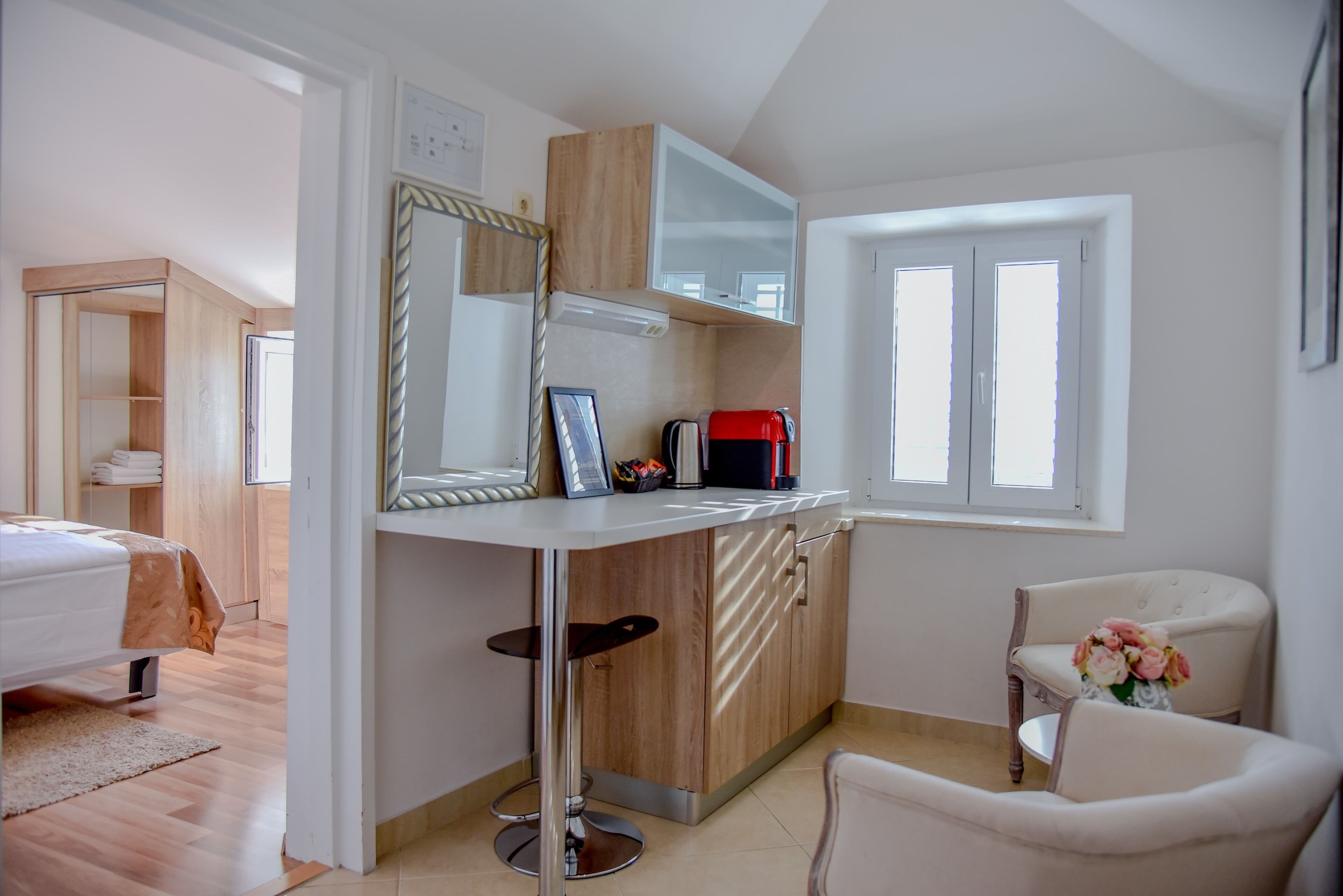 Una habitación de hotel moderna con cama, kitchenette pequeño, espejo y ventana.
