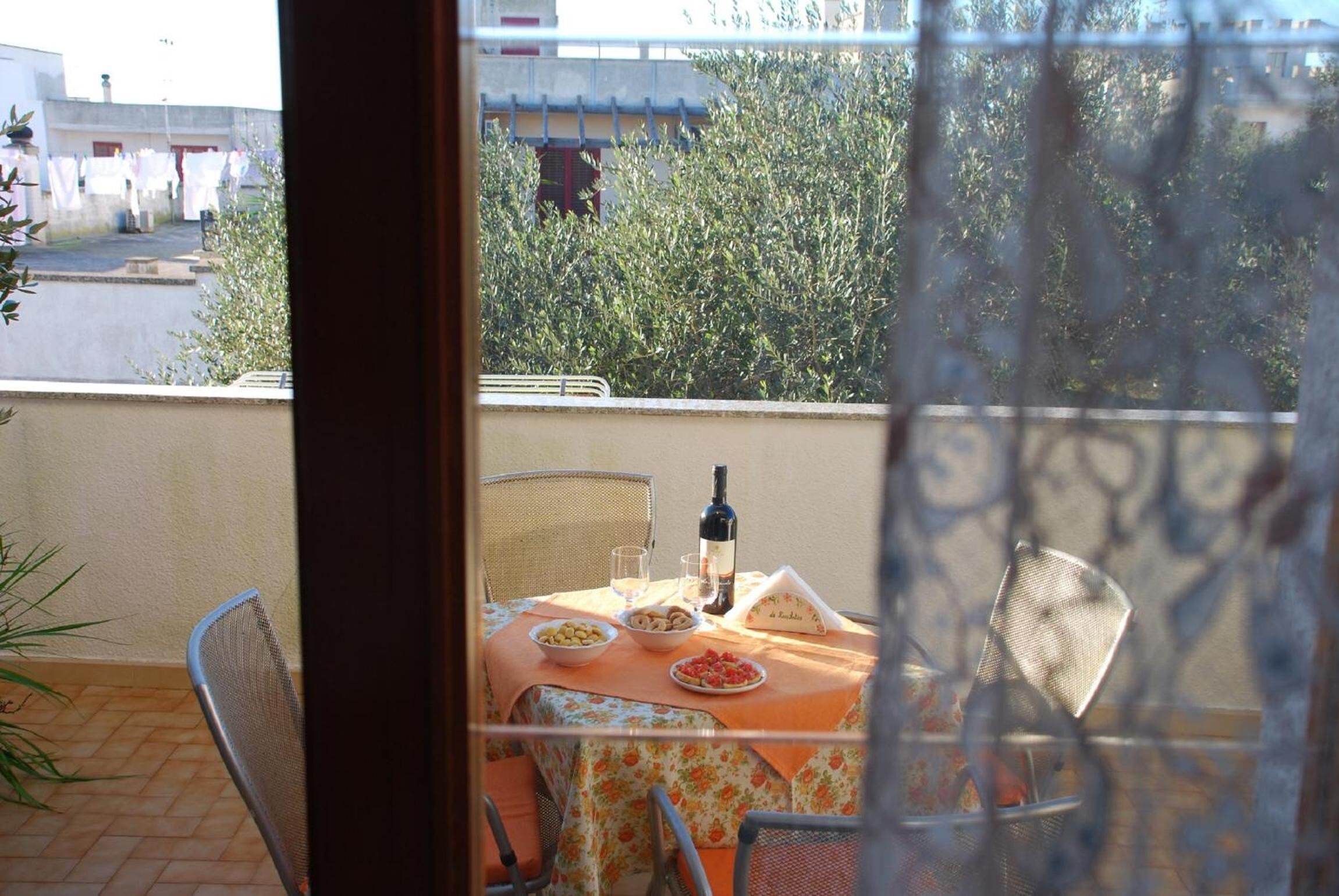 Un balcón con una mesa dispuesta para dos personas, que incluye una botella de vino, copas y platos con comida.