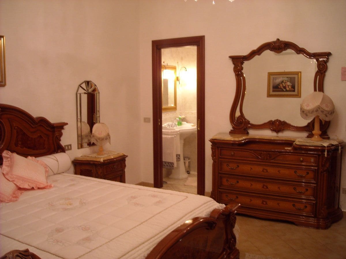 A bedroom with a wooden bed, a dresser, a mirror, and a bathroom visible through an open door.