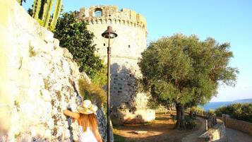 A historic stone wall with a person leaning against it, a lamp post, and a view of a castle-like structure in the background.