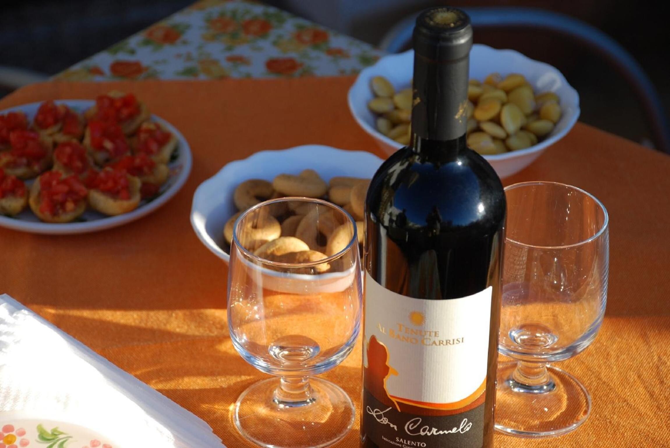 A bottle of wine, two glasses, and plates of food on a table.