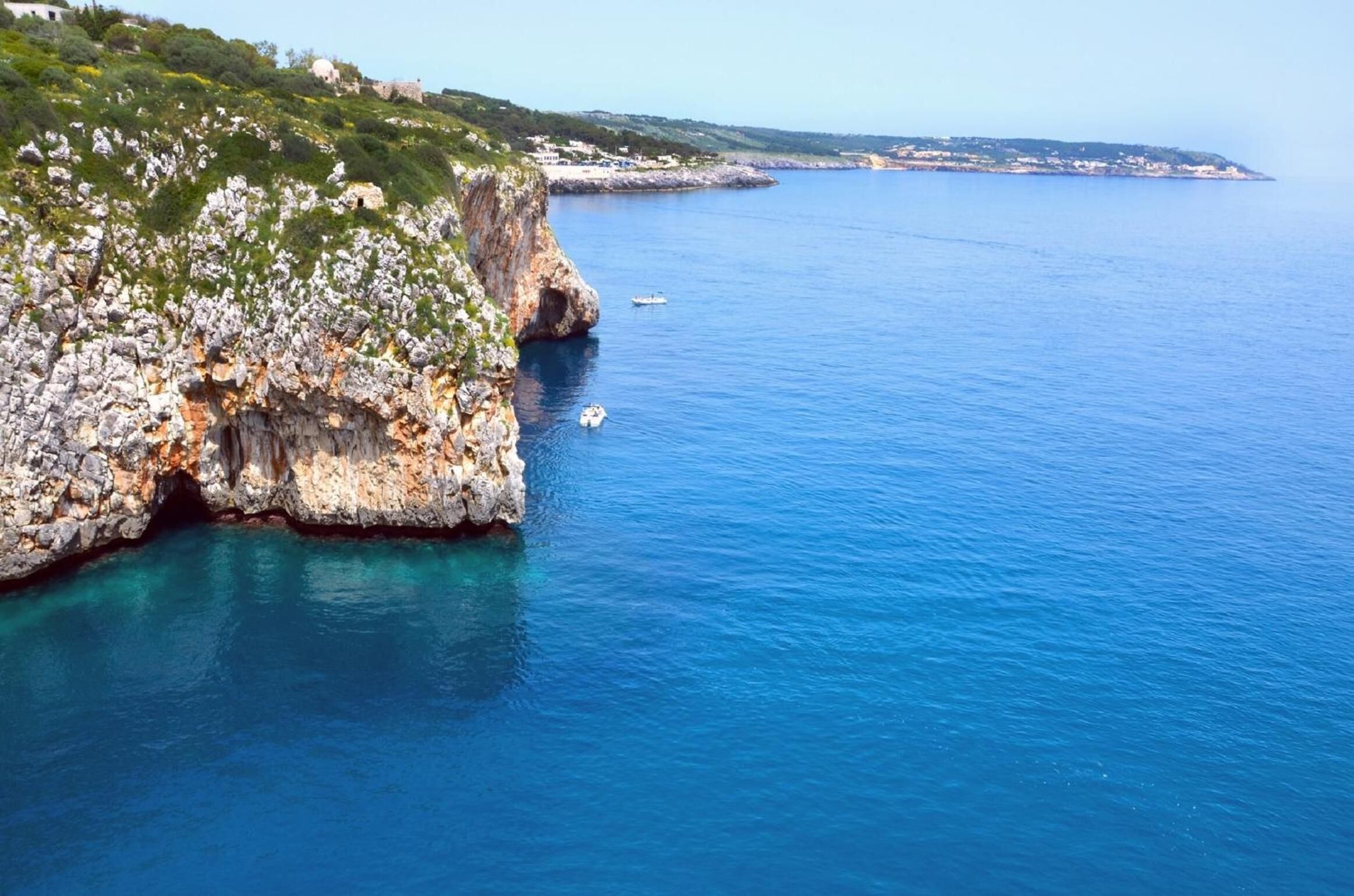 Un paysage côtier avec une falaise rocheuse et une mer d’un bleu limpide.