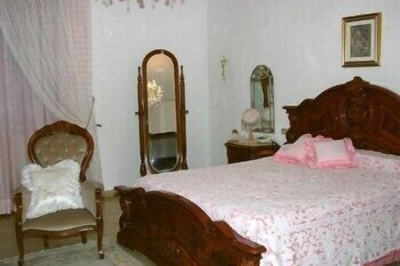 Une chambre à coucher avec un lit en bois, une chaise, un miroir et une table de chevet.