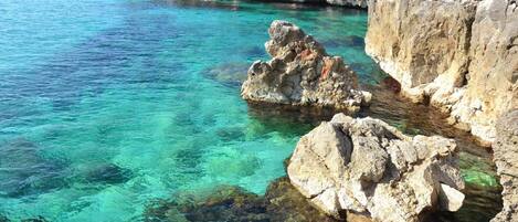 A coastal scene with clear turquoise water, rocky formations, and a rugged coastline.