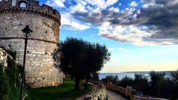 Una torre de piedra histórica con un camino empedrado que la conduce, rodeada de vegetación y un cielo despejado.