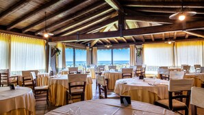 Un restaurante con mesas redondas, sillas y vista al mar.