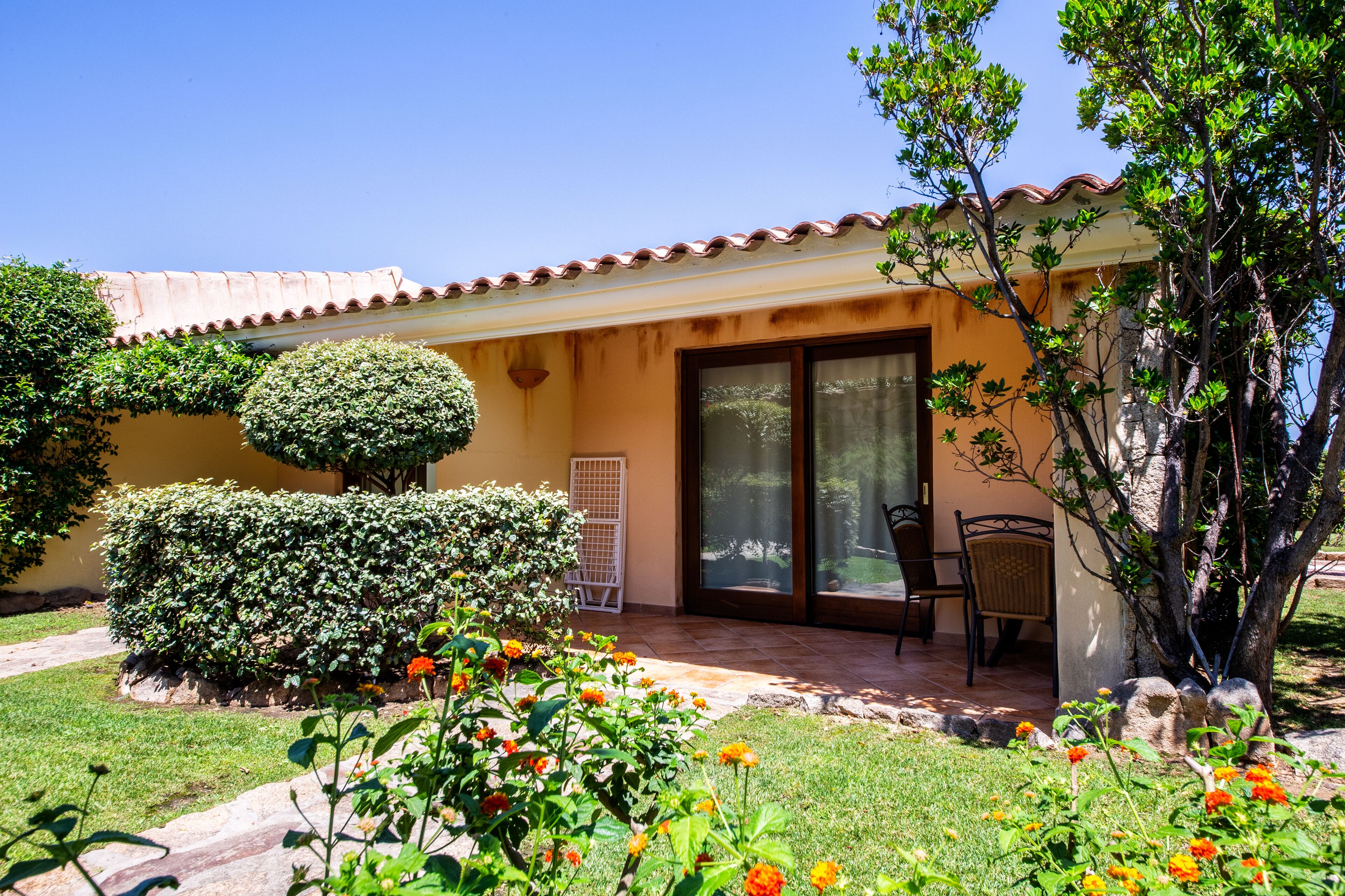A house with a tiled roof, a covered patio, and a garden with flowers and shrubs.