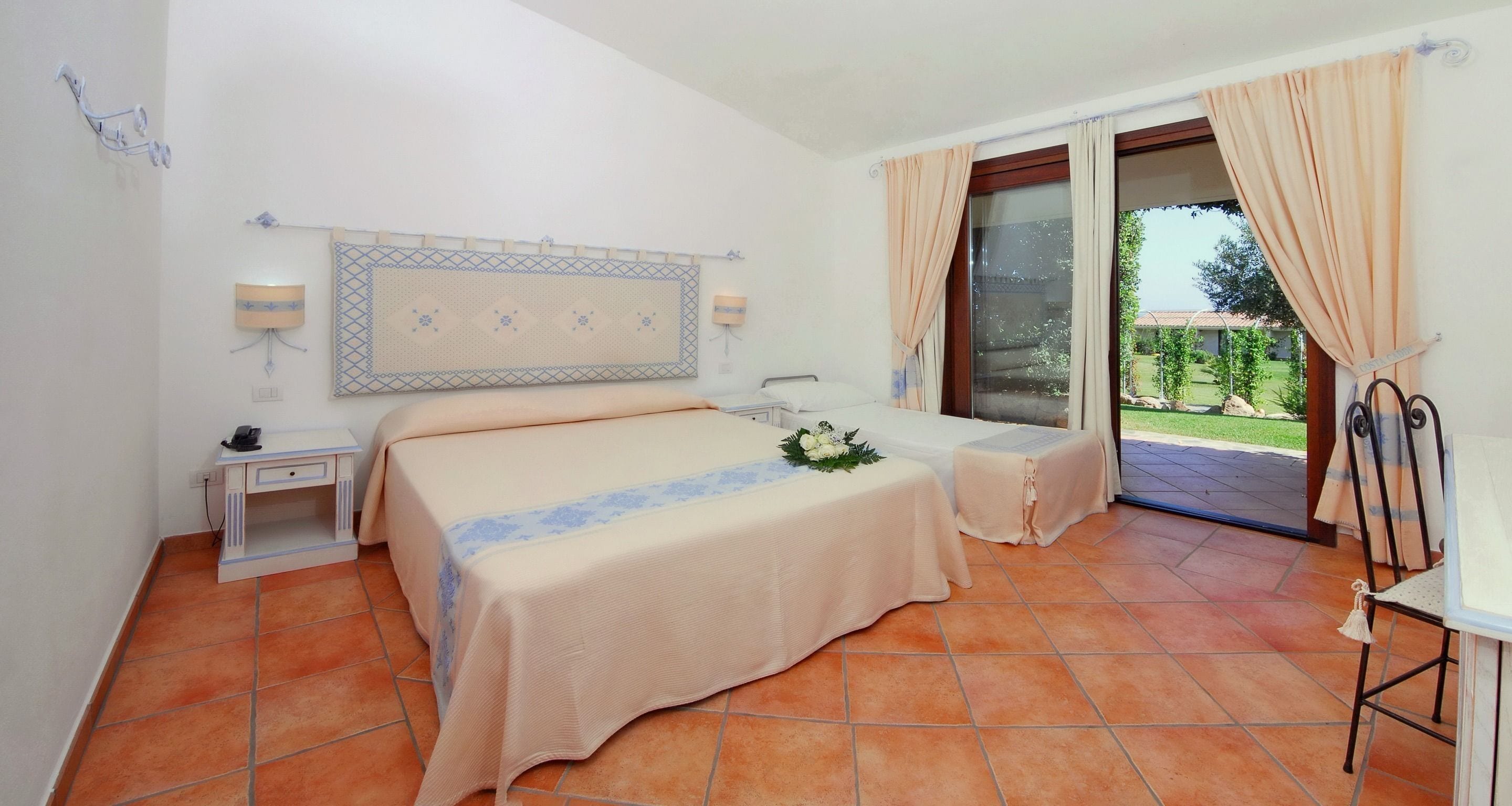 Ein Hotelzimmer mit einem großen Bett, einem kleinen Tisch, einem Sessel, einem Schreibtisch und Blick ins Freie.
