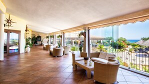 Un espacio interior amplio con suelo de baldosas, muebles de mimbre y ventanas grandes con vistas al mar.