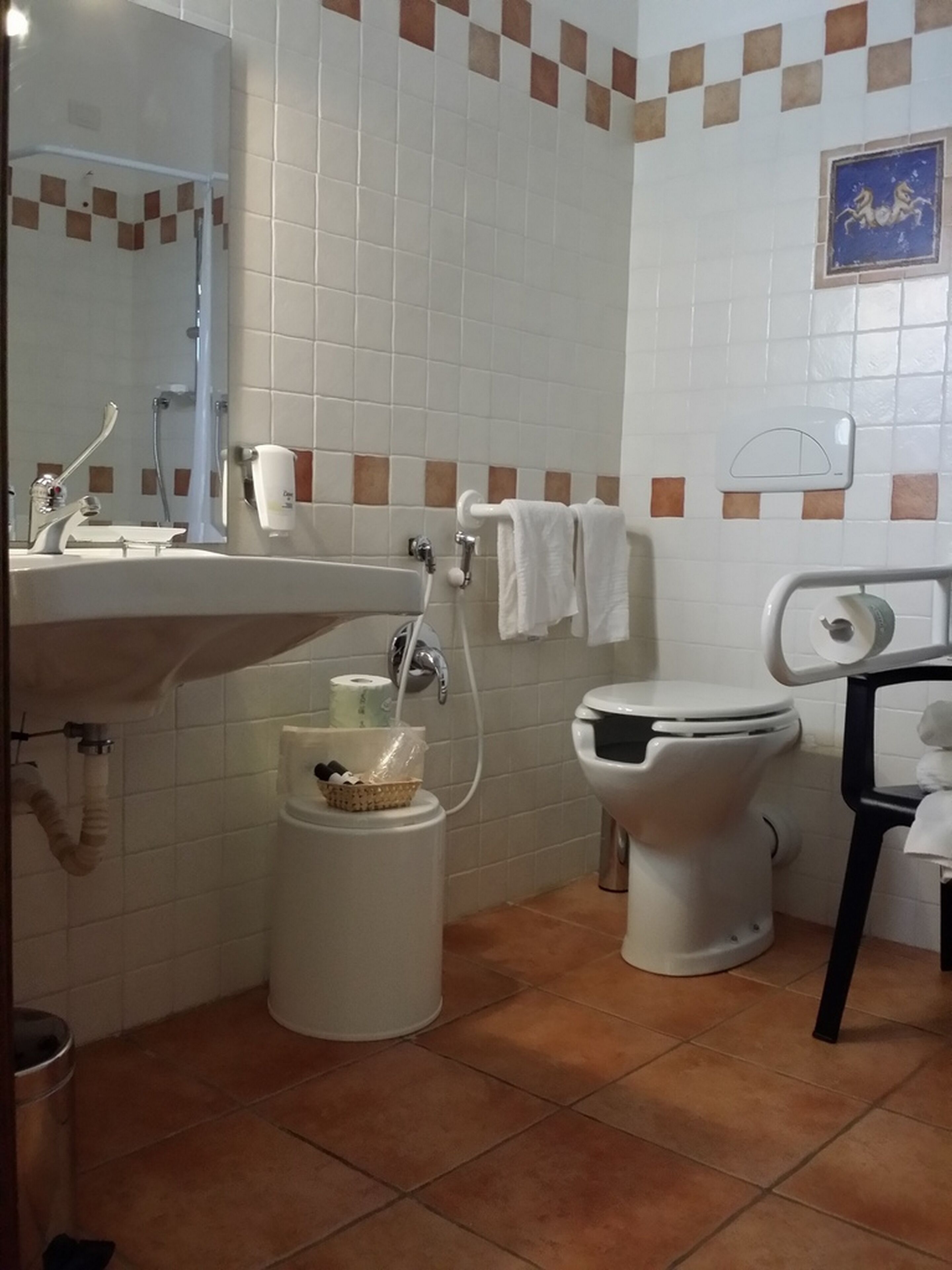 A bathroom with a sink, mirror, toilet, and a trash bin.