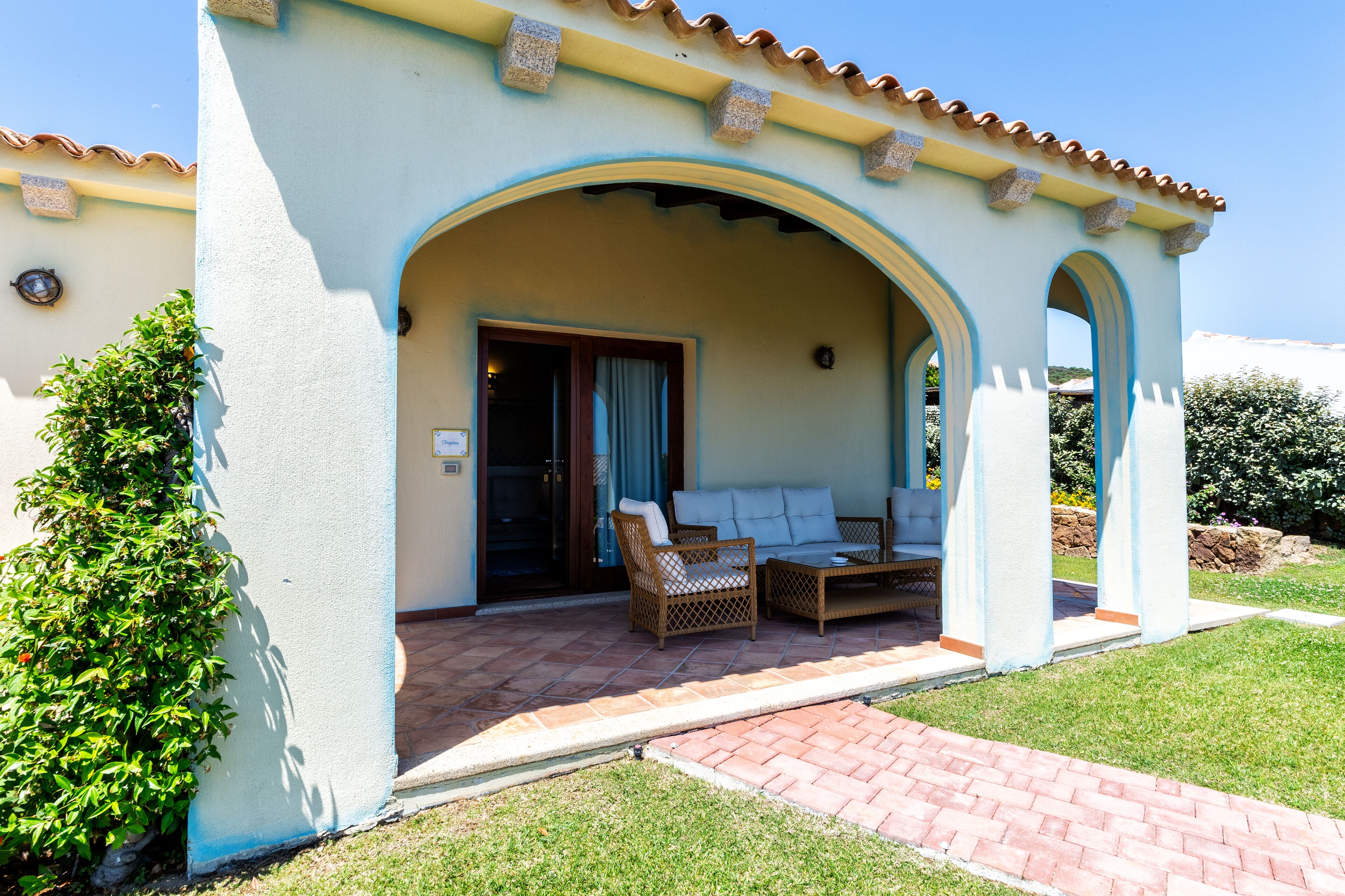 A covered outdoor seating area with a sofa and chairs, a tiled patio, and a stone archway.