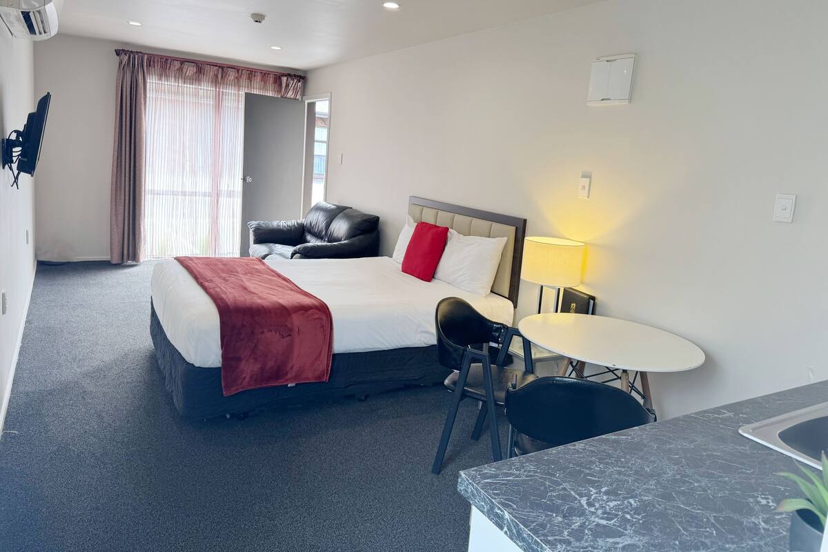 A hotel room with a bed, a desk, a chair, a lamp, and a wardrobe.