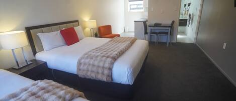A hotel room with a large bed, two bedside tables with lamps, a desk with a chair, and a small table with a chair.