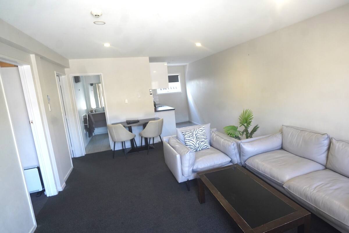 A modern living room with a sofa, a coffee table, and a dining area with chairs.