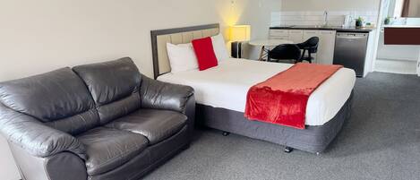 A hotel room with a bed, a leather sofa, a desk with a chair, a microwave, and a small kitchen area.