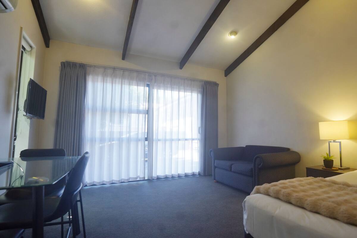 A hotel room with a bed, a desk, a chair, a lamp, and a window with curtains.