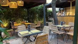 An outdoor seating area with wicker chairs and tables, a menu board, and a bar area in the background. - Ostello 7 Santi (Florence)