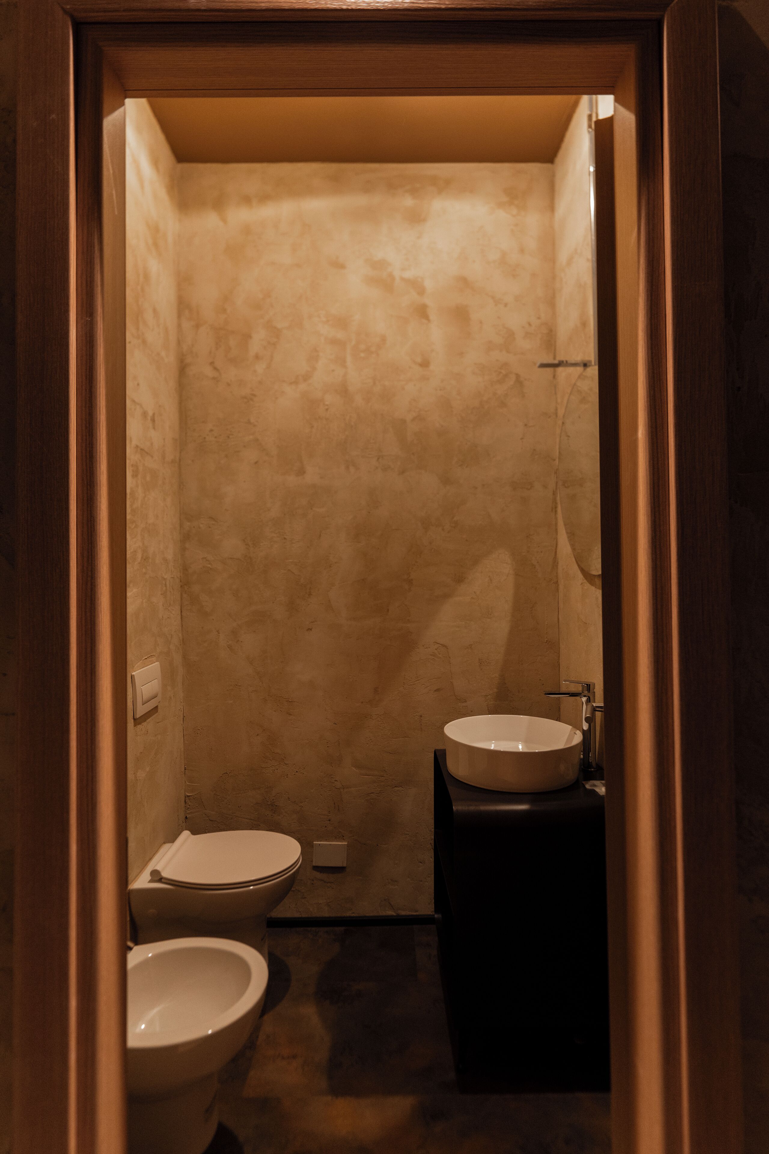 A small, narrow bathroom with a toilet, bidet, and sink.