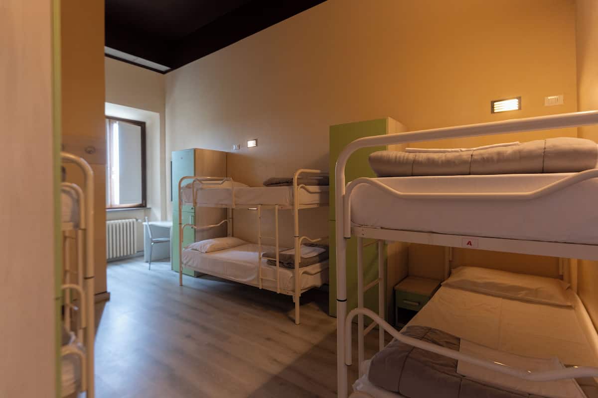 A dormitory room with bunk beds, a radiator, and a window.
