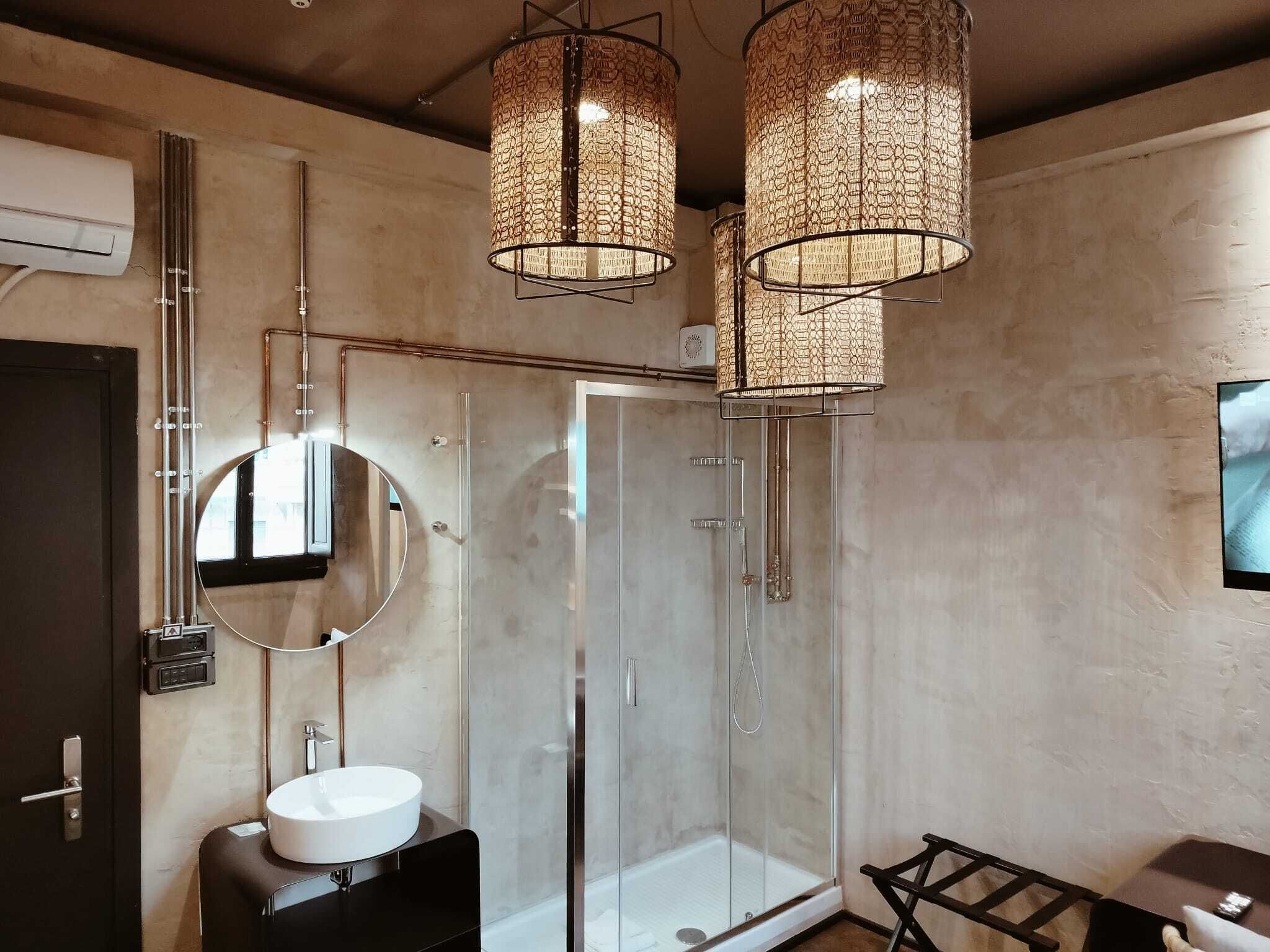 Un baño moderno con cabina de ducha de vidrio, un espejo redondo, un lavamanos blanco y dos lámparas colgantes.