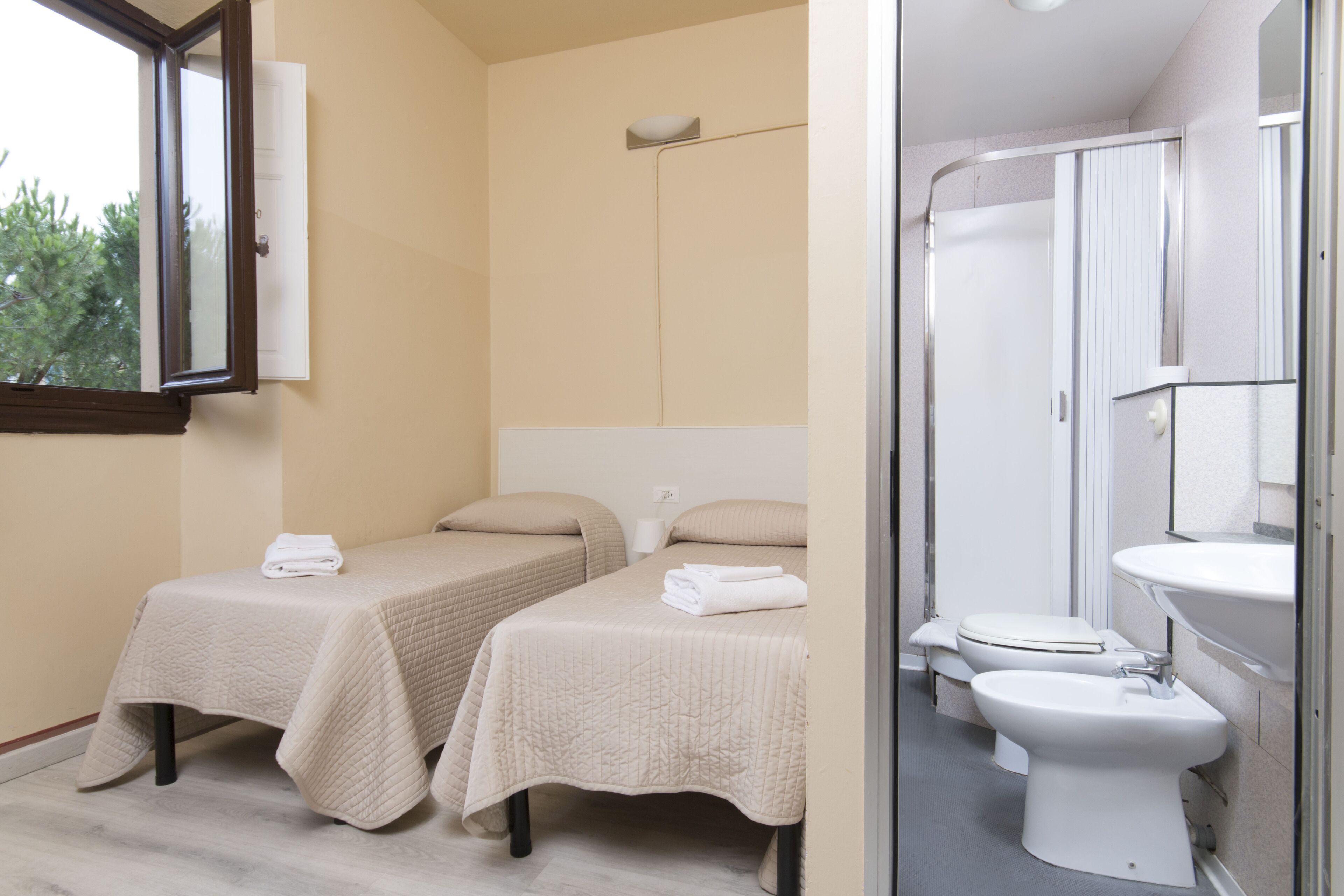 A room with two beds, a window, a shower, and a sink.