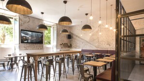 A modern restaurant with high tables and chairs, a large TV screen, and a mural on the wall. - Ostello 7 Santi (Florence)