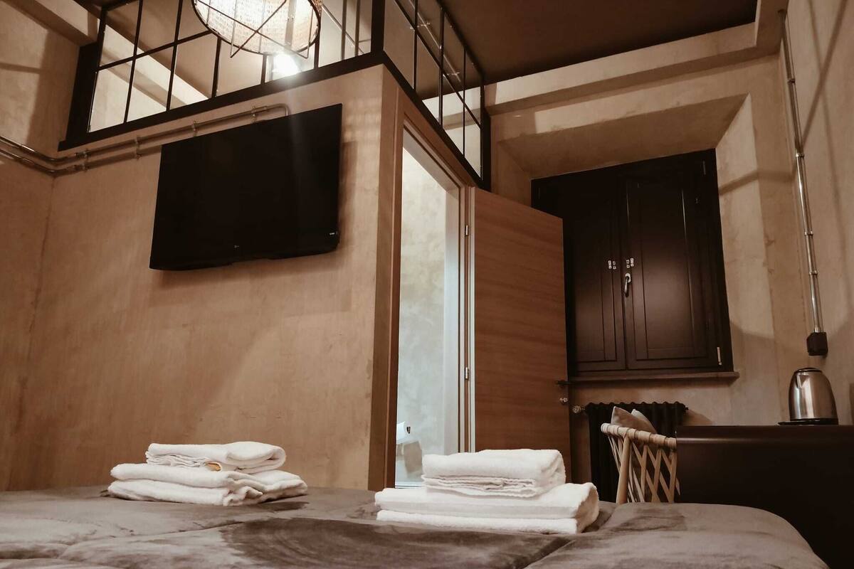 A bedroom with a bed, a TV mounted on the wall, a wooden cabinet, and a kettle on the side table.