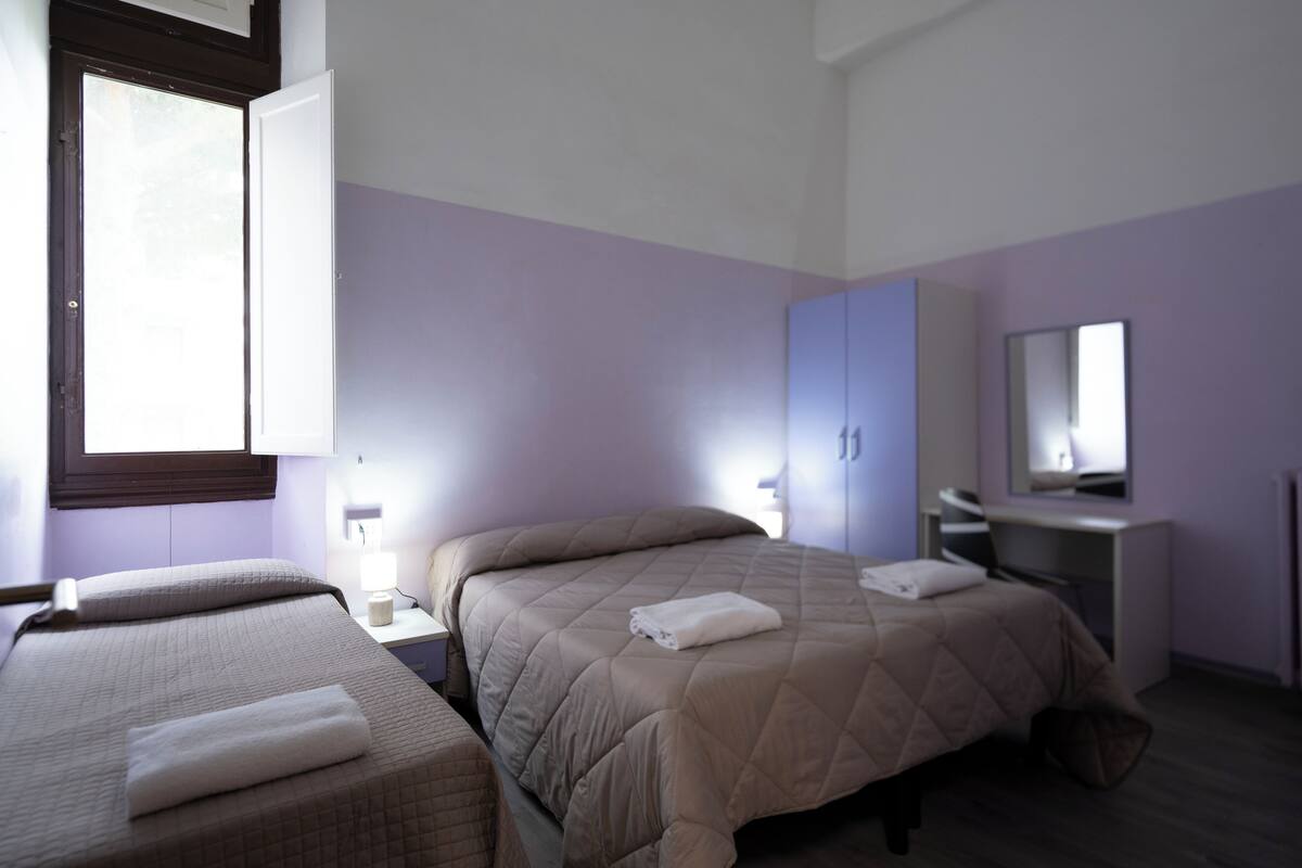 A bedroom with two beds, a desk, and a mirror.