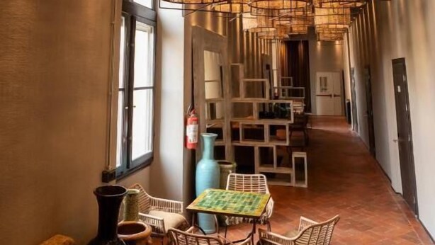 A hallway with wicker pendant lighting, a seating area with a table and chairs, and a view of the corridor. - Ostello 7 Santi (Florence)
