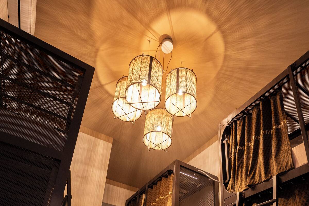 A modern interior with a unique ceiling design, a central chandelier, and a series of bunk beds with curtains.