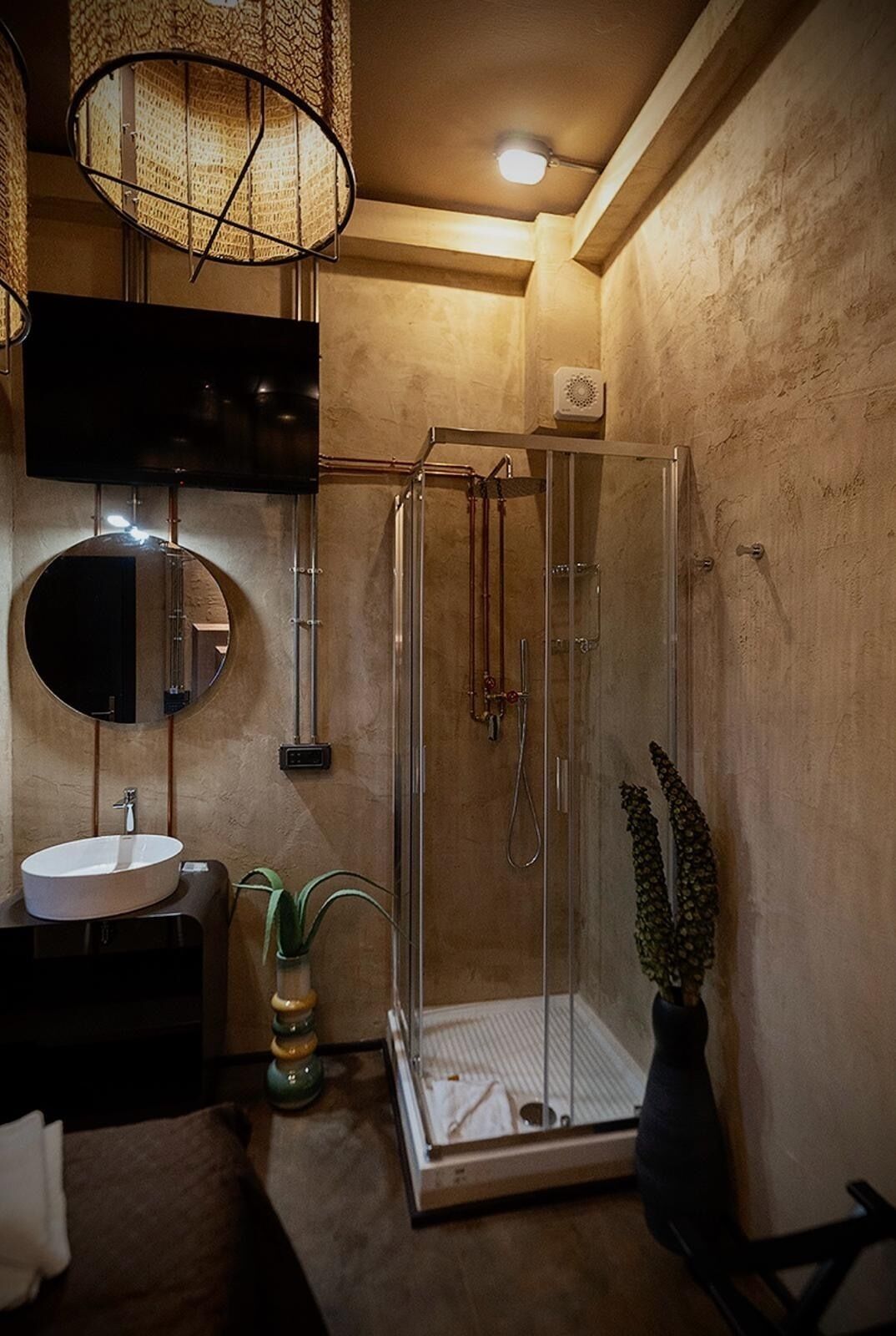 Une salle de bain moderne avec une douche à parois de verre, un miroir rond, un lavabo et un luminaire suspendu.